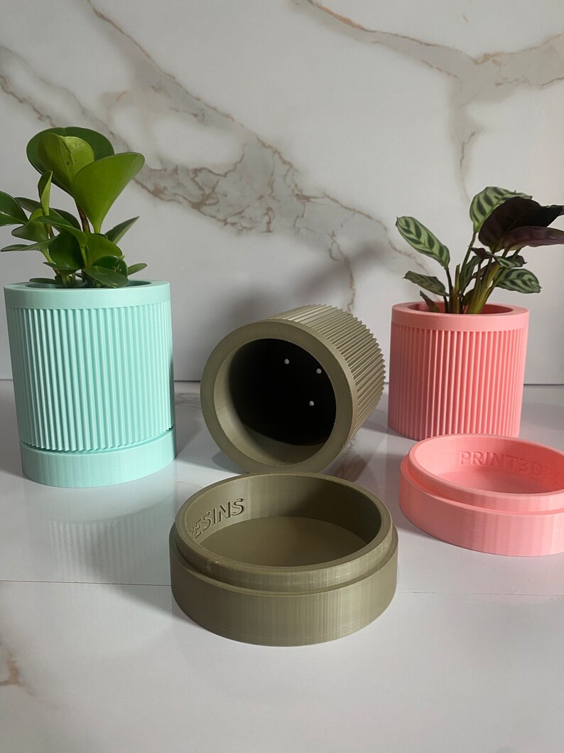 Puede incluir: Cuatro macetas para plantas impresas en 3D en diferentes colores: azul claro, rosa, verde y marr&oacute;n. Las macetas tienen un dise&ntilde;o acanalado y todas son del mismo tama&ntilde;o. Las macetas est&aacute;n sobre una superficie de m&aacute;rmol blanco. El texto "PRINTED" es visible en la maceta rosa y el texto "DESIGNS" es visible en la maceta verde.