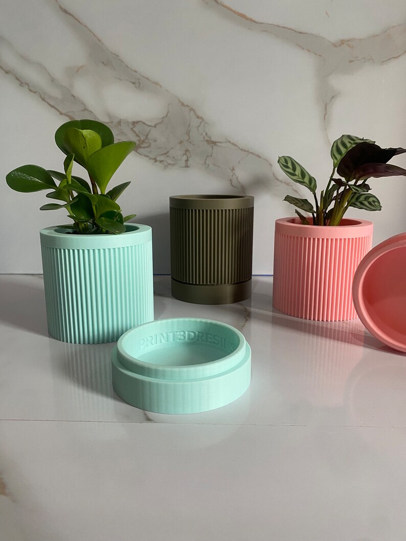 Puede incluir: Tres macetas de plantas acanaladas en diferentes colores: azul claro, verde oscuro y rosa. Las macetas est&aacute;n hechas de un material texturizado y tienen una forma ligeramente redondeada. La maceta azul claro tiene un platillo a juego.