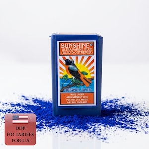 Könnte beinhalten: Ein rechteckiger blauer Behälter mit Sunshine Ultramarinblau Pigmentpulver. Das Etikett zeigt eine Vogelillustration vor einem Sonnenaufgang mit dem Text Sunshine Ultramarine Blue, Original Blue und Made under arrangement with Polypex Ltd.