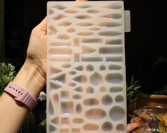 May include: A clear silicone mold with various shapes for resin casting. The mold features a variety of geometric shapes, including circles, ovals, squares, rectangles, triangles, and hearts.