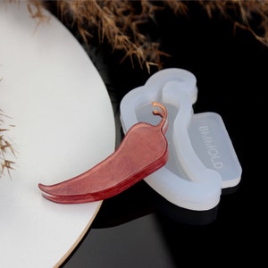 May include: A red chili pepper resin casting with a clear, shiny finish. The casting is next to a silicone mould with the word "BMMOLD" printed on it.