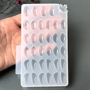 May include: A clear silicone mold with 34 elongated cavities for resin jewellery making. The mold has a leaf-shaped detail and text that reads "SILICONE MOLD" and "34 in-1 Elongated Mold - For Resin - Jewelry Making."