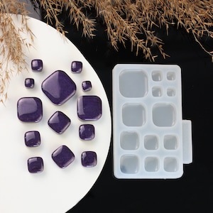 May include: A silicone mould with 15 square-shaped cavities for making resin jewellery. The mould is white and has a clear, transparent appearance. There are 15 purple resin pieces in the image, which are square and rectangular in shape.