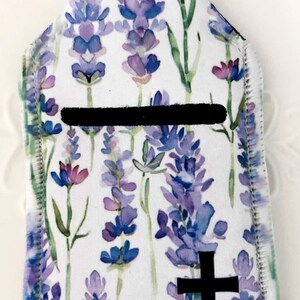 May include: A white key fob with a lavender floral pattern and a black cross. The design features purple and blue lavender flowers with green stems. A black horizontal stripe is across the centre. A silver metal ring is at the top.