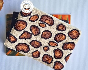May include: A white clutch purse with a brown and orange leopard print design. The purse is made with a fluffy, textured fabric and has a small, round tag that says "Handmade with Love".
