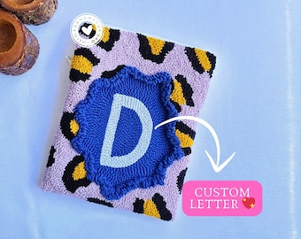 May include: A pink and yellow leopard print pouch with a blue and white custom letter D in the centre. The pouch is handmade with love.