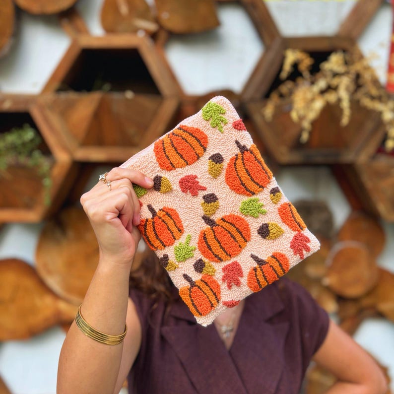 May include: A pink fabric pouch with a repeating pattern of orange pumpkins, green leaves, and brown acorns.