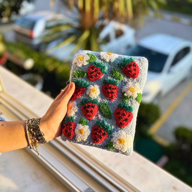 Peut inclure: Une pochette bleue avec un motif r&eacute;p&eacute;t&eacute; de fraises brod&eacute;es et de fleurs blanches. La pochette est faite d'un tissu doux et textur&eacute;.