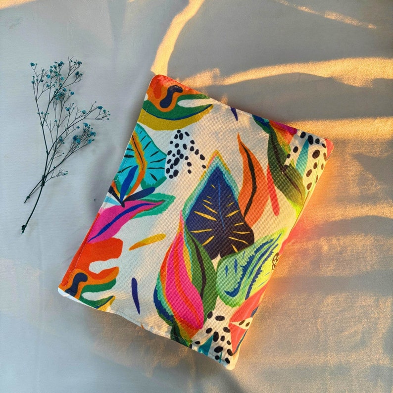 May include: A white canvas pouch with a colorful abstract floral print. The print features bright pink, blue, green, and yellow colors. The pouch is perfect for carrying small items like makeup, jewelry, or phone.