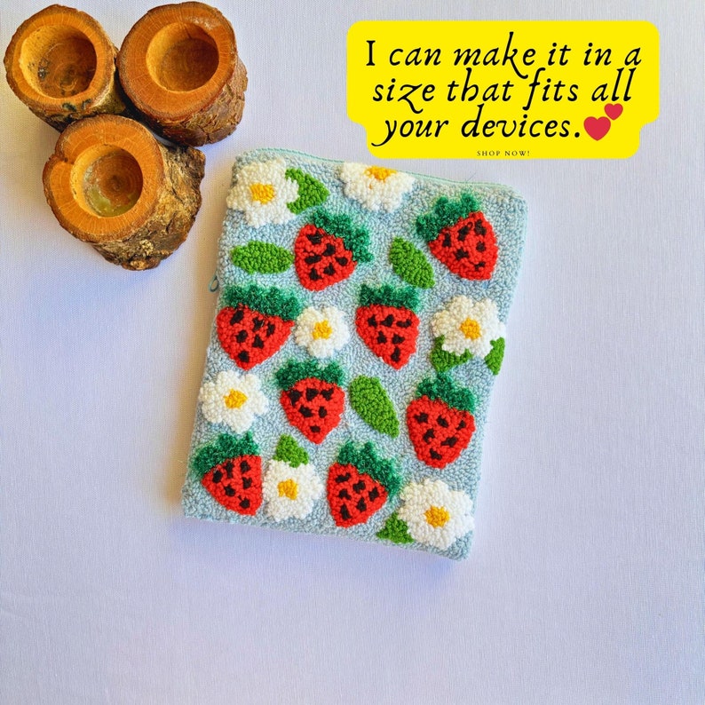Peut inclure: Une pochette bleue avec une fermeture &eacute;clair pr&eacute;sente un motif r&eacute;p&eacute;t&eacute; de fraises rouges, de fleurs blanches et de feuilles vertes. Le texte "I can make it in a size that fits all your devices. SHOP NOW!" est imprim&eacute; sur un fond jaune.