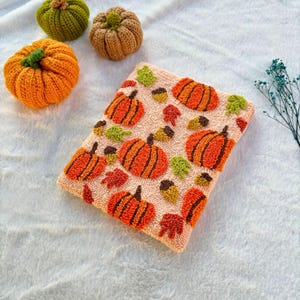 May include: A pink and white rug with a pattern of orange and brown pumpkins, green leaves, and acorns. The rug is made with a fluffy, textured yarn.