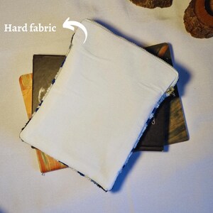 May include: A white zippered pouch with a hard fabric lining. The pouch is lying on top of two books.