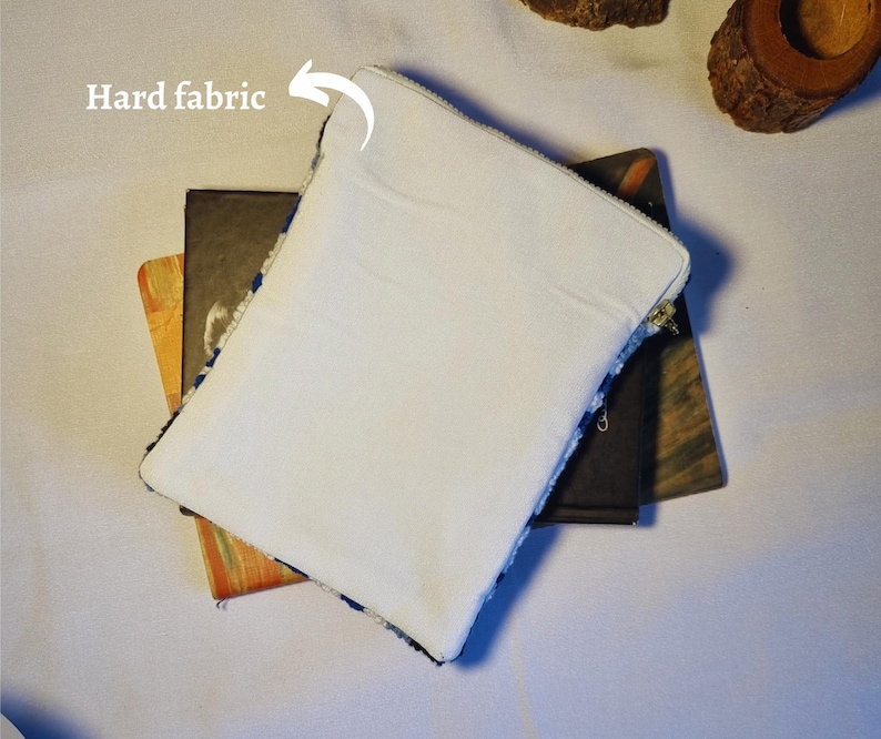 May include: A white zippered pouch with a hard fabric lining. The pouch is lying on top of two books.