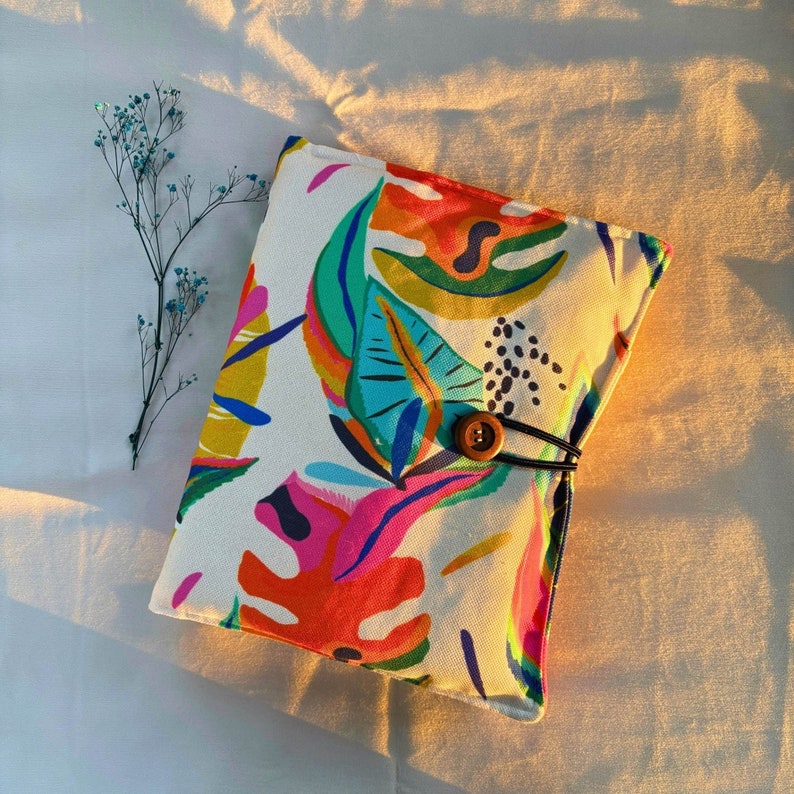 May include: A white canvas pouch with a colorful abstract floral print and a brown button closure. The pouch is made of a soft, durable fabric and has a unique, modern design.