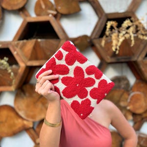 May include: A white clutch with a red floral pattern. The flowers are raised and have a fluffy texture.