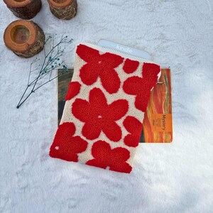 May include: A white and red floral patterned pouch with a zipper closure. The pouch is large enough to hold a Kindle e-reader. The text "kindle" is visible on the e-reader.