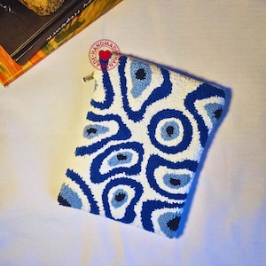 May include: A white pouch with a blue and white eye pattern. The pouch is handmade and has a zipper closure.