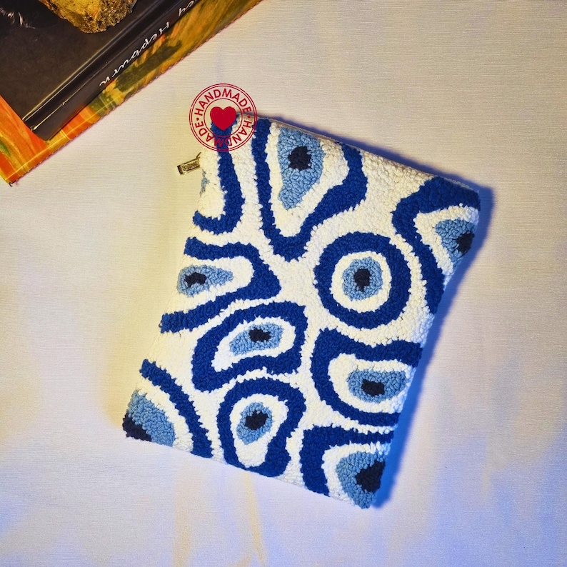 May include: A white pouch with a blue and white eye pattern. The pouch is handmade and has a zipper closure.