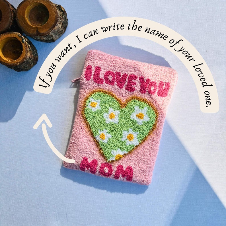 May include: Pink fuzzy pouch with a green heart embroidered with white daisies and the words "I LOVE YOU MOM" in pink.