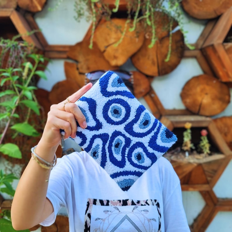 May include: A white and blue clutch bag with a swirling pattern of blue eyes. The bag is made of a soft, plush material and has a unique, eye-catching design.