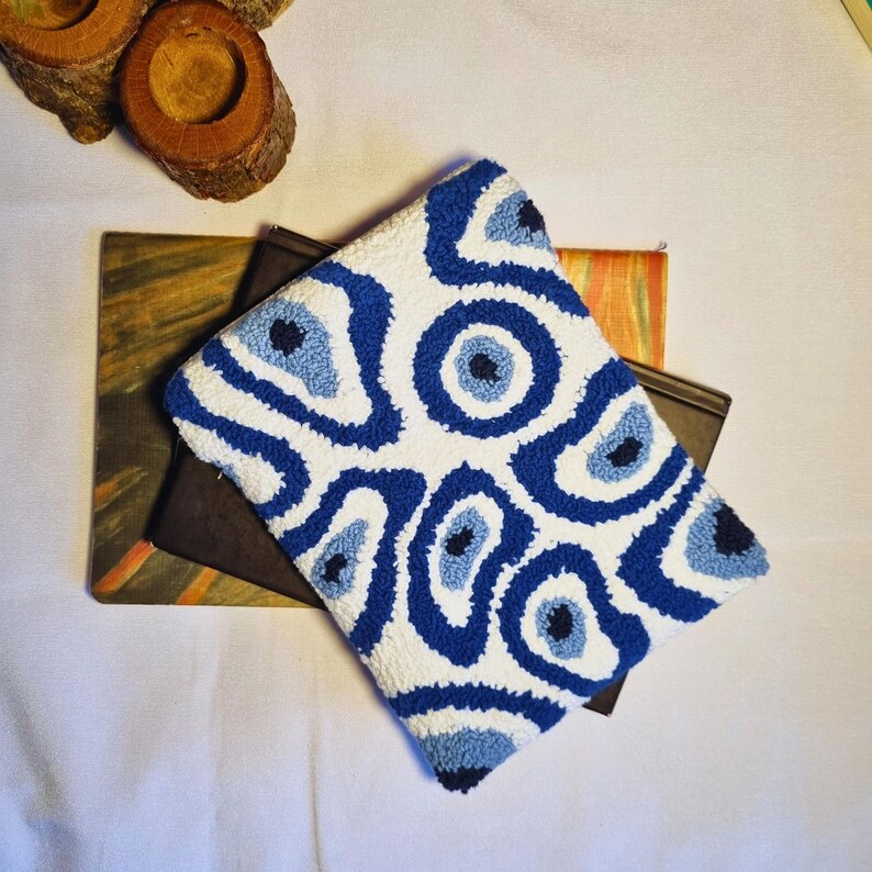 May include: A white and blue patterned cushion with a design of stylized eyes. The cushion is made of a soft, textured fabric.