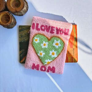 May include: Pink pouch with a green heart with white flowers and the text "I LOVE YOU MOM" in pink letters.