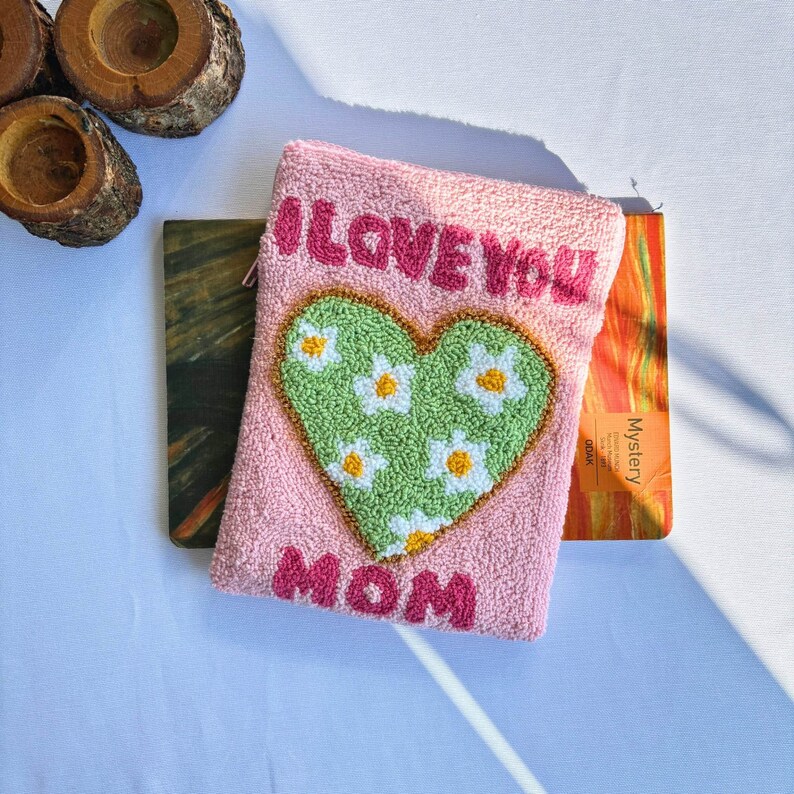 May include: Pink pouch with a green heart with white flowers and the text "I LOVE YOU MOM" in pink letters.
