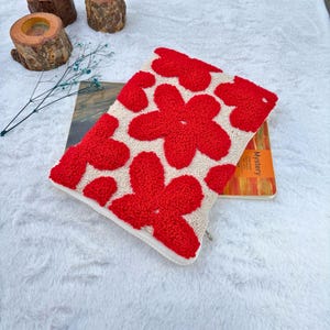 May include: A white zippered pouch with a red floral design. The pouch is made of a soft, plush fabric and has a zipper closure.