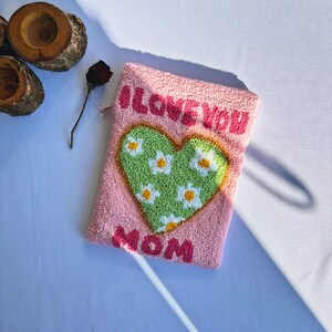May include: Pink fabric pouch with a green heart with white flowers and the words "I Love You Mom" embroidered on it.
