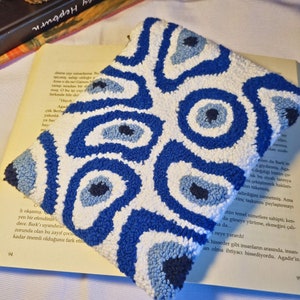May include: A white pouch with a blue and white evil eye pattern. The pouch is made of a soft, textured fabric and is perfect for holding small items.
