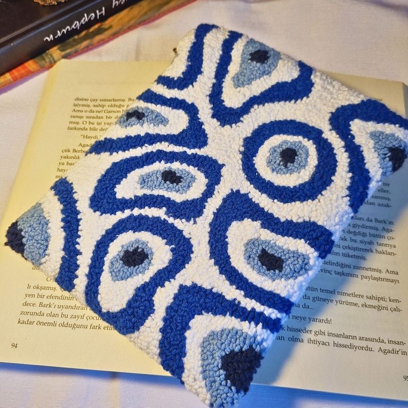 May include: A white pouch with a blue and white evil eye pattern. The pouch is made of a soft, textured fabric and is perfect for holding small items.