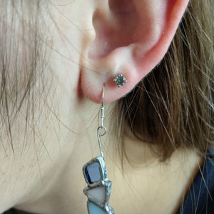 May include: A pair of silver dangle earrings with three triangular pieces of glass. The glass pieces are blue, pink, and light blue. The earrings are hanging from a silver hook.