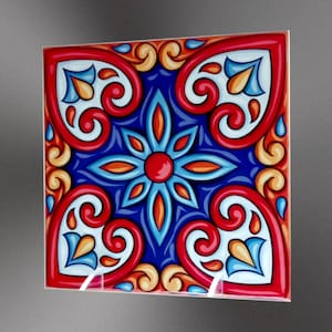 May include: A square ceramic tile with a blue, red, orange, and white geometric pattern. The tile features a central flower design with four curved, heart-shaped designs in the corners.