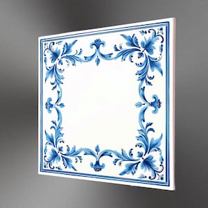 Op de afbeelding: Vierkante witte tegel met een blauwe bloemenrand. Het ontwerp toont sierlijke bladeren en krullen. De tegel is schuin, wat de dikte en een glimp van de zijkant laat zien.