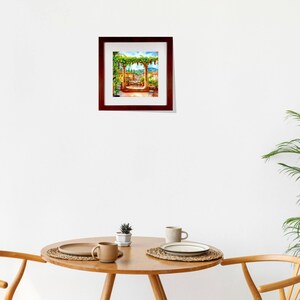 May include: A framed watercolor painting depicts a sunny outdoor scene with a pergola covered in green vines. The painting features a table and chairs, with a view of a town and blue sky. The frame is a dark brown color.