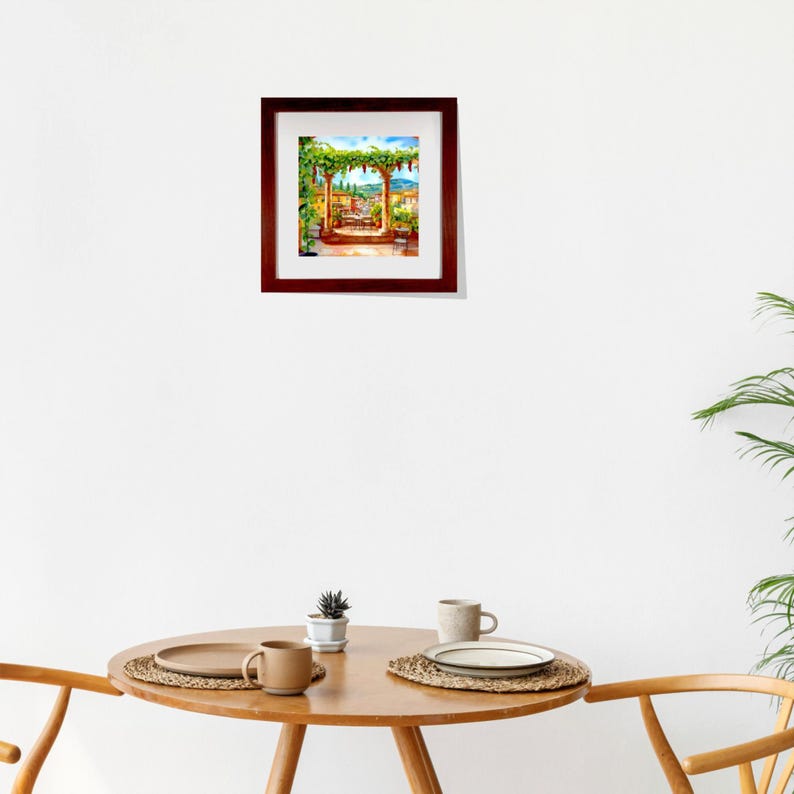May include: A framed watercolor painting depicts a sunny outdoor scene with a pergola covered in green vines. The painting features a table and chairs, with a view of a town and blue sky. The frame is a dark brown color.