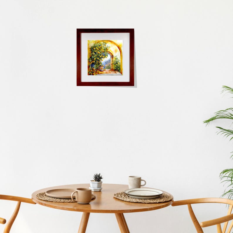 Op de afbeelding: Een ingelijst aquarel schilderij van een gele boog met een citroenboom die er doorheen groeit. De boog leidt naar een uitzicht op een blauwe lucht en bergen in de verte.