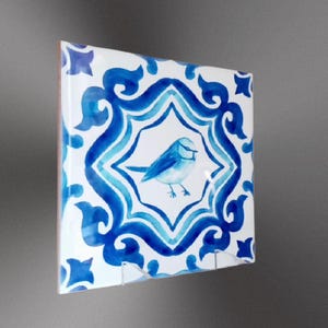 May include: A blue and white ceramic tile featuring a blue bird design. The tile has a traditional Moroccan pattern.