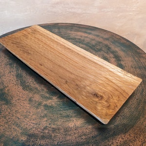 Könnte beinhalten: Ein rechteckiges Holztablett mit einer natürlichen Holzoptik. Das Tablett hat einen leicht abgerundeten Rand und ein rustikales Aussehen.