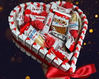 May include: A heart-shaped arrangement of assorted chocolate bars, including Kinder, Bueno, and Kinder Cards, decorated with red roses. The arrangement is held by a hand with a red ribbon.
