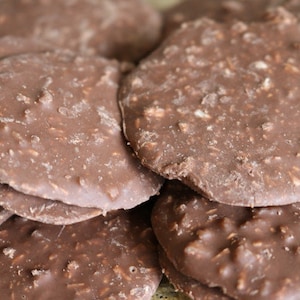 Op de afbeelding: Een close-up van een stapel chocolade-kokoskoekjes. De koekjes zijn rond en hebben een licht ruwe textuur. Ze zijn lichtbruin van kleur en hebben een glanzende afwerking.