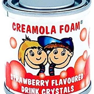 Könnte beinhalten: Eine Metalldose mit Creamola Foam Erdbeer-Aroma-Getränkekristallen. Die Dose zeigt eine Cartoon-Illustration von zwei lächelnden Kindern und den Text "Strawberry Flavoured Drink Crystals". Die Dose ist weiß mit roten und rosa Akzenten.
