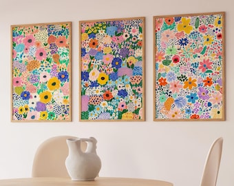 May include: Three framed prints featuring colourful floral patterns, displayed in a contemporary dining room setting. The prints are hung on a white wall above a wooden table with four beige chairs.
