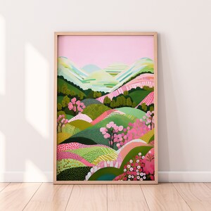 Pode incluir: Uma impressão de arte emoldurada com uma paisagem colorida. A obra de arte mostra colinas onduladas em tons de verde, rosa e branco, com árvores e um céu rosa. A moldura é feita de madeira clara.