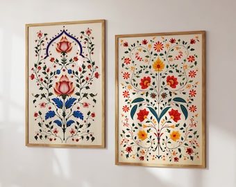 May include: Two framed floral prints with intricate designs. The print on the left features a central flower with red and pink petals and blue leaves. The print on the right features a central flower with red petals and yellow leaves. Both prints have a white background and are framed in natural wood.