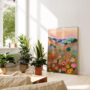 May include: A framed art print featuring a colorful landscape with rolling hills and a vibrant field of flowers. The artwork has a gold frame and is displayed in a bright, airy room with potted plants.