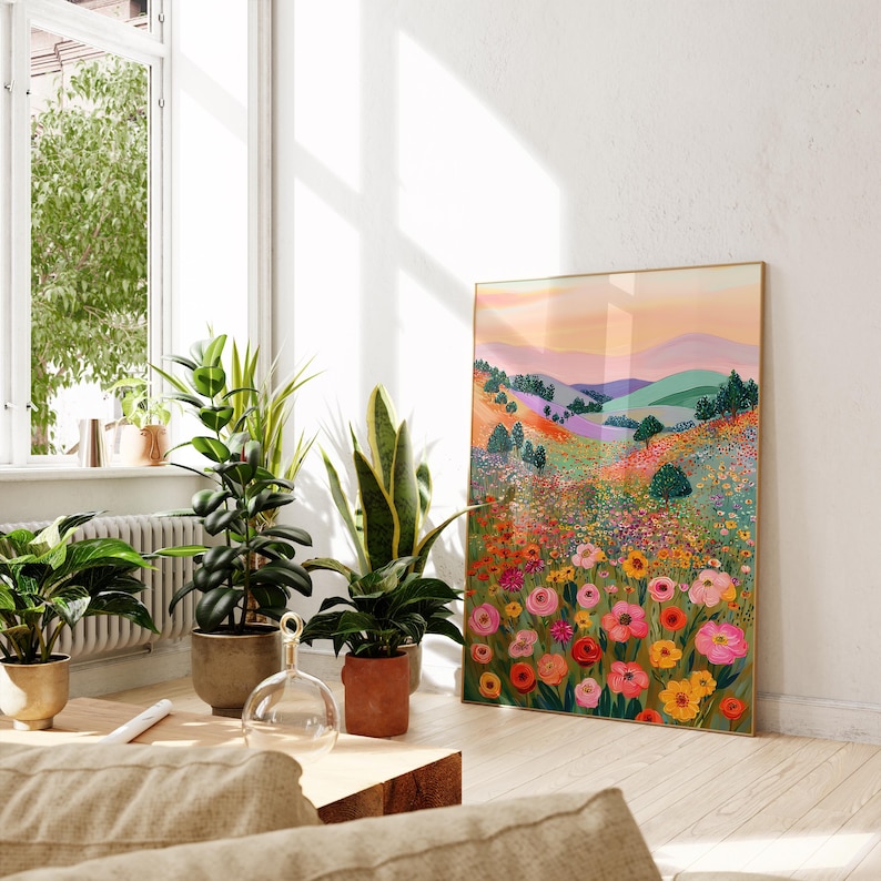 May include: A framed art print featuring a colorful landscape with rolling hills and a vibrant field of flowers. The artwork has a gold frame and is displayed in a bright, airy room with potted plants.