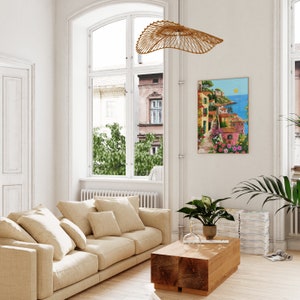 May include: A beige sofa with multiple pillows in a living room with a large window, a wooden coffee table, and a painting of a colorful Italian village on the wall.