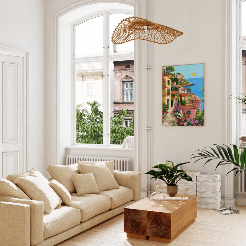 May include: A beige sofa with multiple pillows in a living room with a large window, a wooden coffee table, and a painting of a colorful Italian village on the wall.