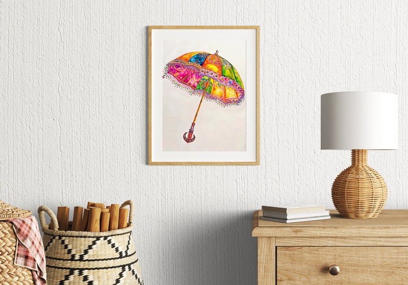 Op de afbeelding: Een ingelijst aquarel schilderij van een kleurrijke, sierlijke paraplu met een houten handvat. De paraplu is geschilderd in tinten roze, geel, groen, blauw en paars. De achtergrond is wit.